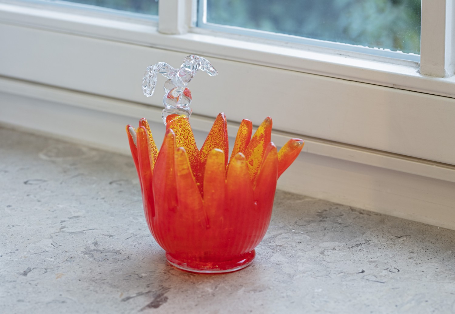 Objekt der aus Glas gefertigten dreiteiligen Objektserie "Fleurs" von Julie Béna. Das Glasobjekt stellt einen roten Blütenkopf dar, auf dem ein Miniaturphallus positioniert ist. Die Arbeit stellt vorherrschende Genderkategorien infrage, indem sie die Konnotationen des Phallussymbols verunsichern.