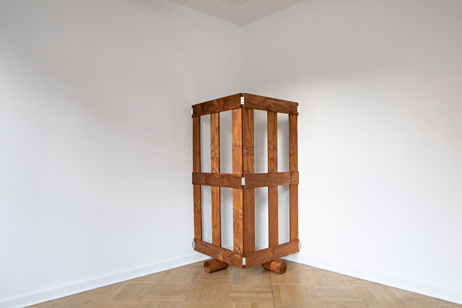 A brown, two-sided wooden gate stands on two wooden rollers. It is attached to the wall with the open sides.